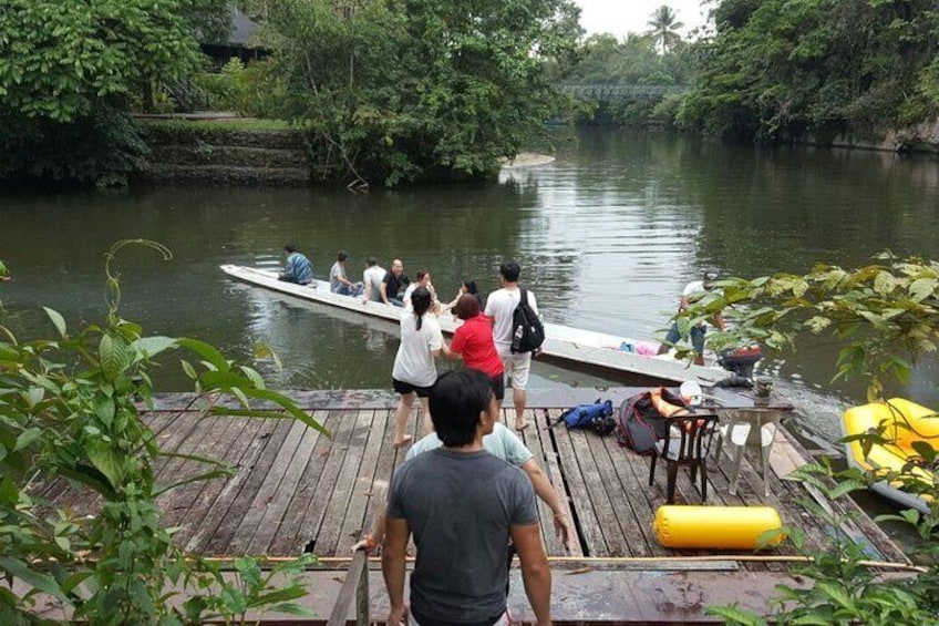 A group of people on a boat docked at a wooden pier with a river and lush greenery in the background. 5