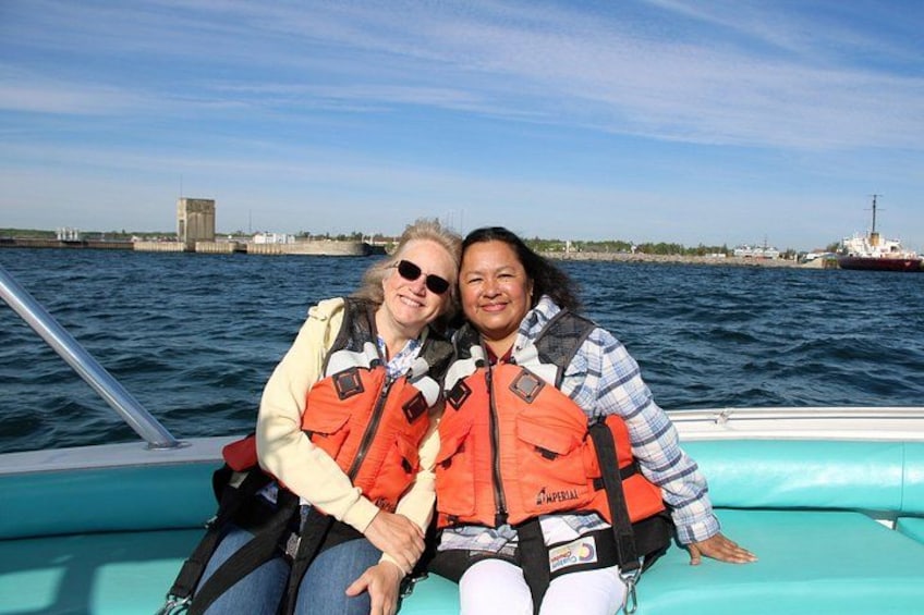 Two people on a boat wearing life jackets, with a body of water and a distant ship in the background. 5