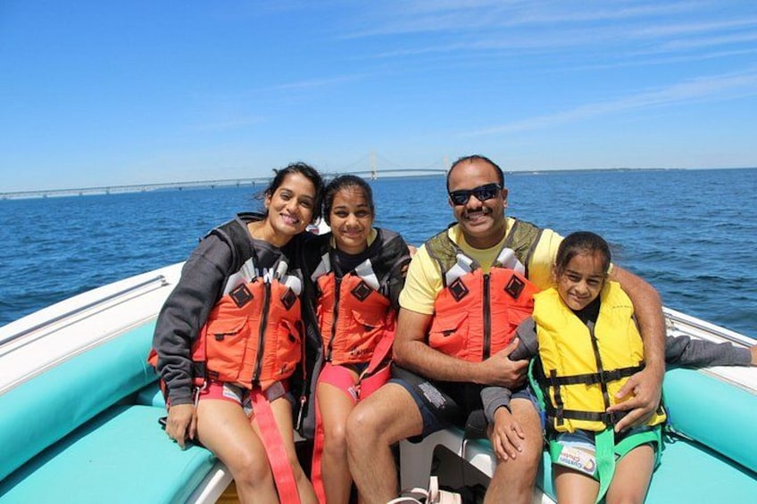 Four people on a boat wearing life jackets, with a bridge in the background. 3