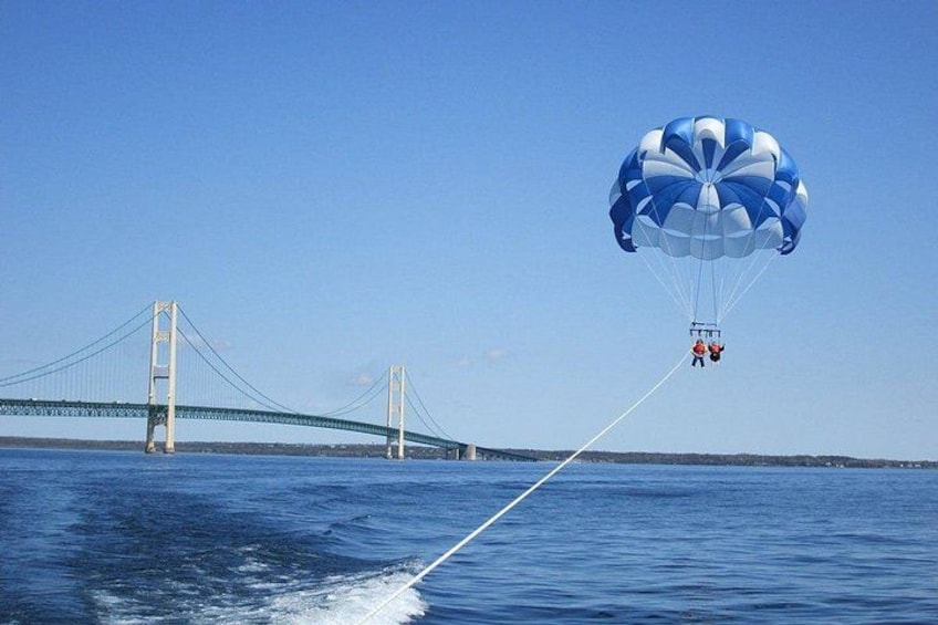 A person parasailing over a body of water with a bridge in the background. 2