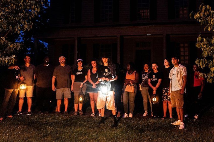 A group of people standing on grass in front of a building at night. 2