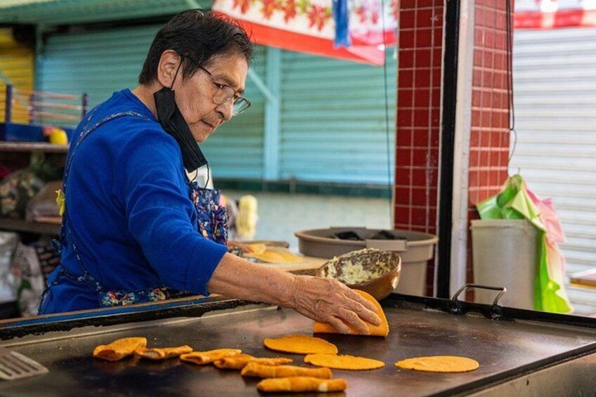 Une personne est en train de cuisiner sur une plaque de cuisson plate, avec des tortillas et un bol à proximité. 2