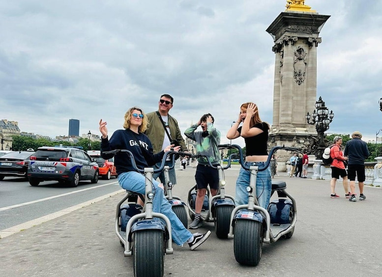 Personas circulando en scooters eléctricos por una calle urbana, con un monumento al fondo. 1