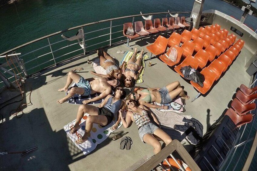 A group of people sunbathing on a boat deck with chairs and a railing. 4