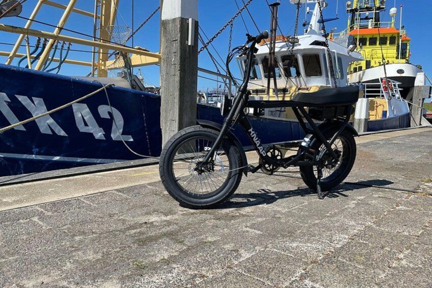 A bicycle parked on a dock with a large ship in the background. 4