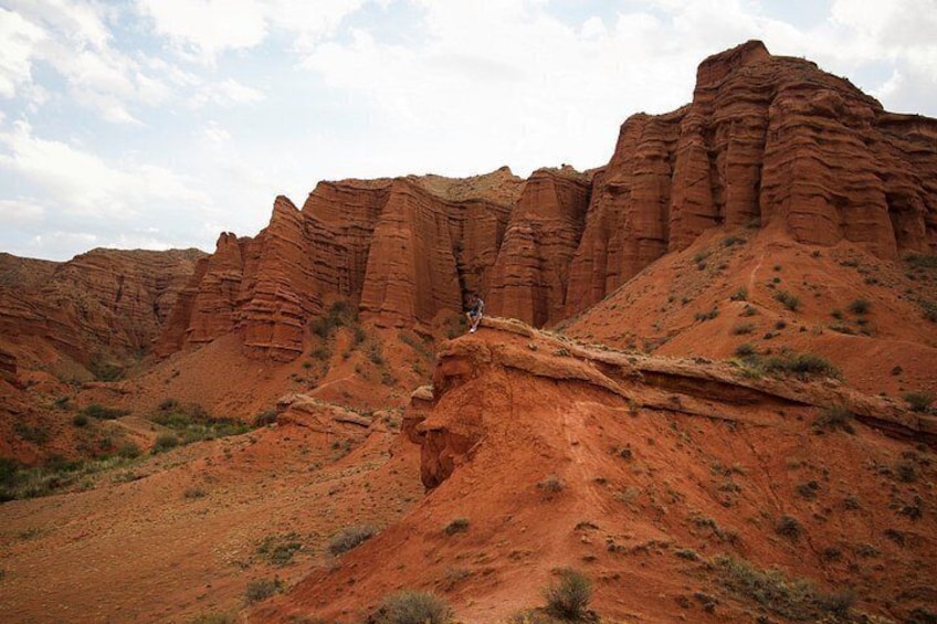 A person hiking on a red rock trail with layered rock formations in the background. 2