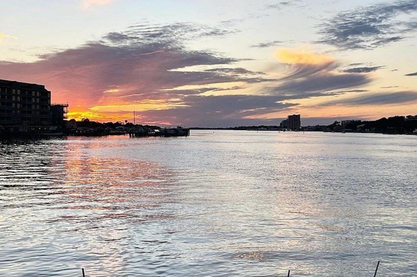 Un atardecer sobre un río tranquilo, con edificios a la izquierda y un muelle que se adentra en el agua. 3