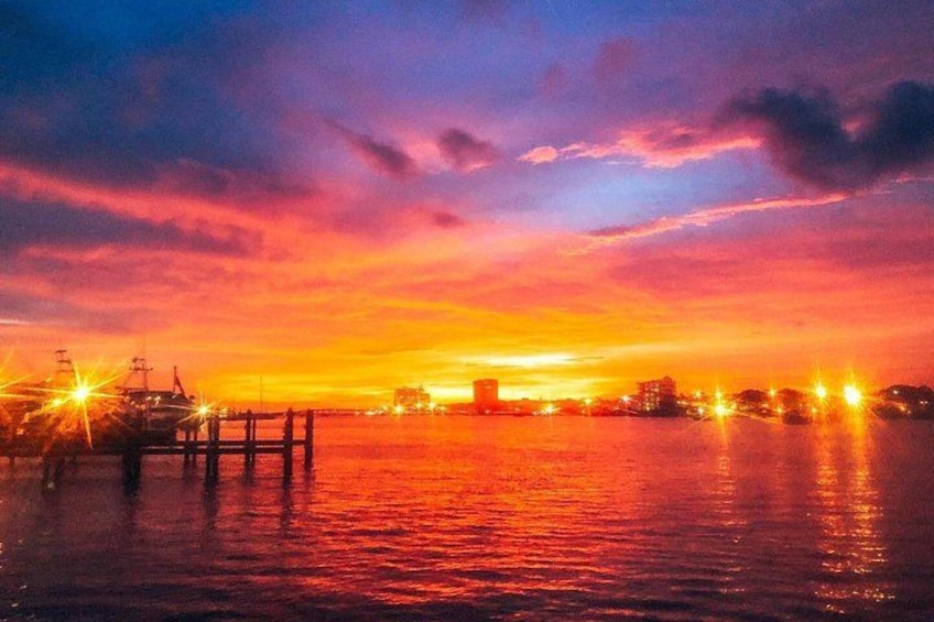 Atardecer sobre una masa de agua con un muelle y luces de la ciudad a lo lejos. 1