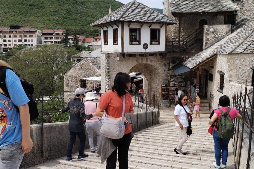 Eine Steinkonstruktion, über die Touristen gehen, ein historisches Gebäude und eine gebirgige Landschaft im Hintergrund. 5