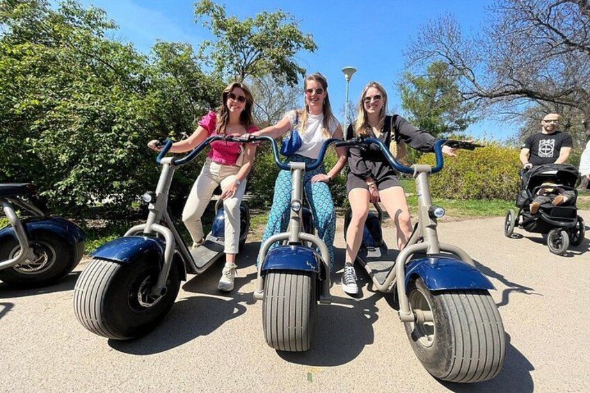 Tres personas circulando en scooters eléctricos por un camino pavimentado, con árboles al fondo. 2