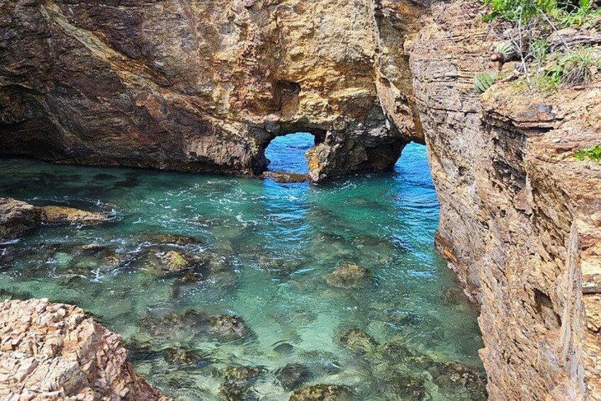 A rocky coastal landscape with clear water, a natural arch formation, and rugged cliffs. 1