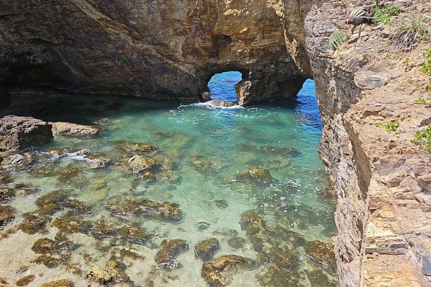A rocky coastal area with clear water, a cave entrance, and a narrow passageway. 4