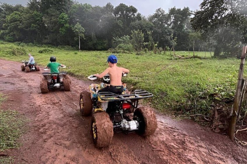 Tre persone guidano quad attraverso un sentiero fangoso immerso nel verde. 2
