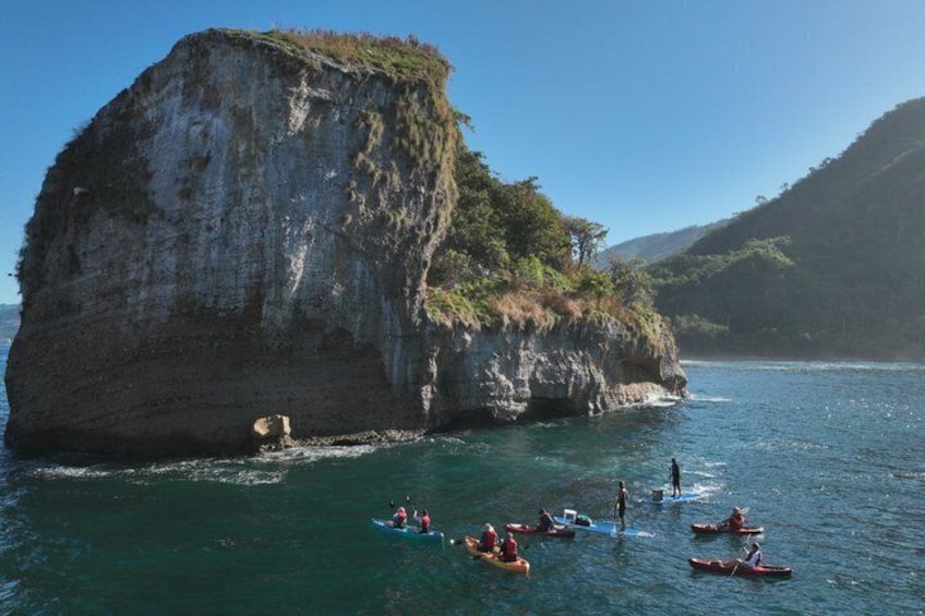 A large rock formation surrounded by water with people kayaking and paddleboarding. 4