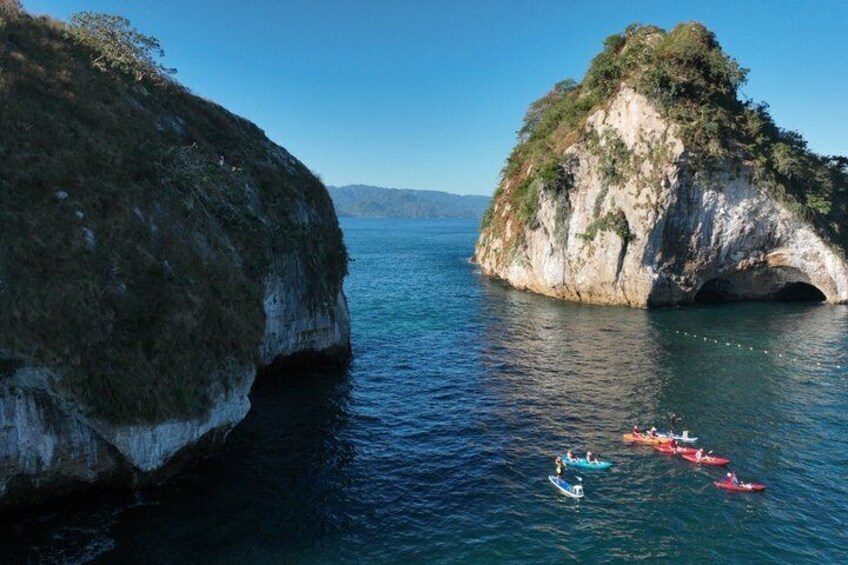 A coastal landscape with large rock formations and kayaks on the water. 3