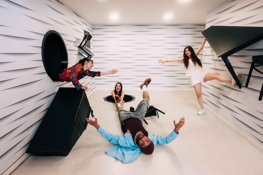 A group of people lying on the floor in a room with white walls and a piano. 1