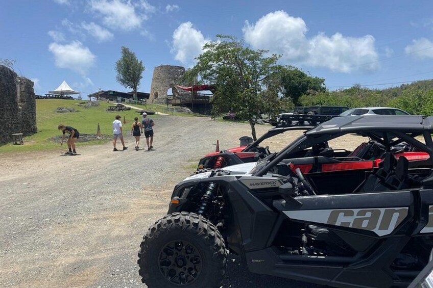 A dirt road with a black ATV and a group of people standing on the side. 1