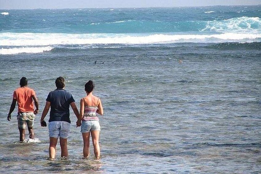 Three people walking in shallow water towards the ocean. 1