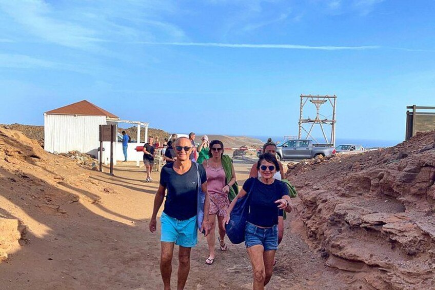 A group of people walking on a dirt path with a rocky landscape and a small building in the background. 2