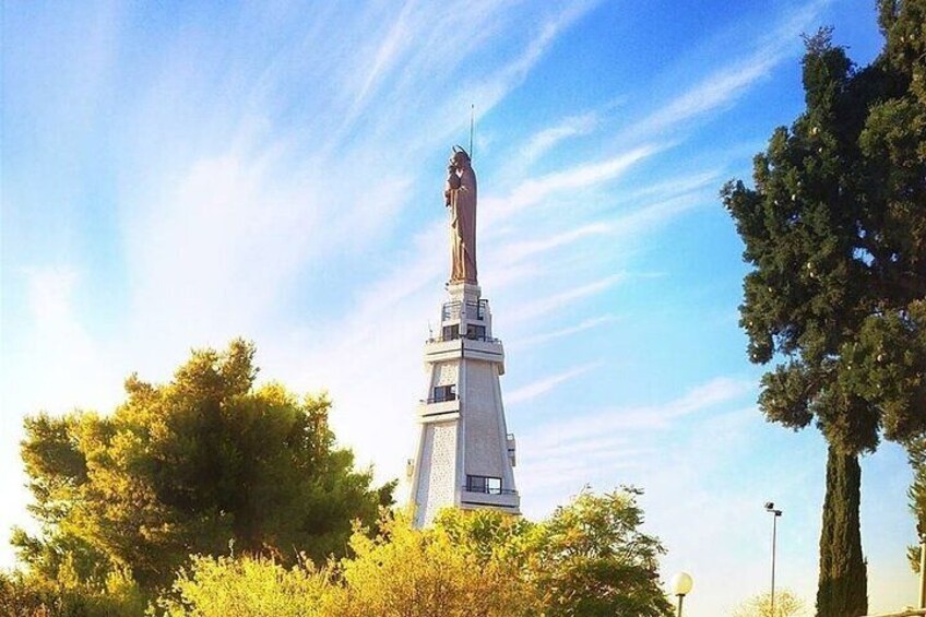 A tall monument with a statue on top, surrounded by trees and a clear sky. 2
