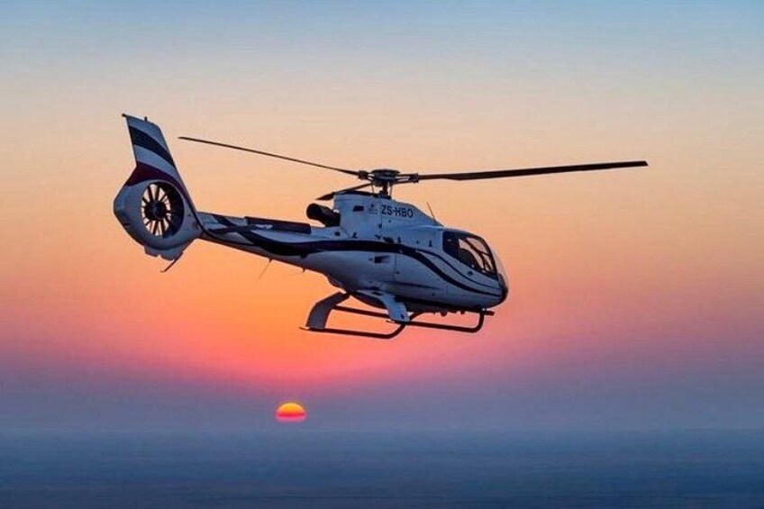 En helikopter flyver over vandet i solnedgangen. 3