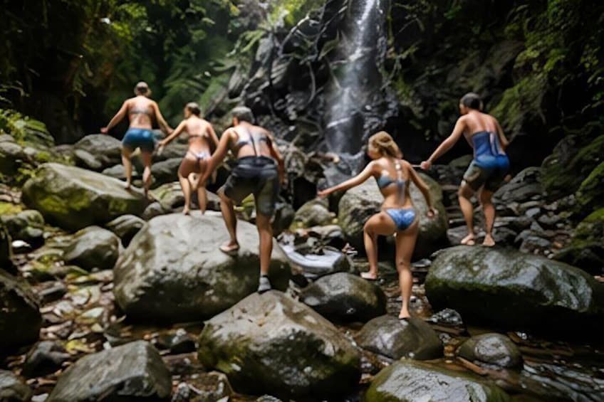 People in swimwear standing on rocks near a waterfall in a forested area. 3