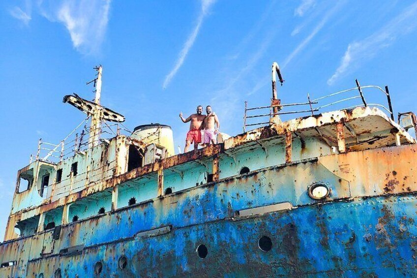 A rusted shipwreck with two people standing on its deck. 2