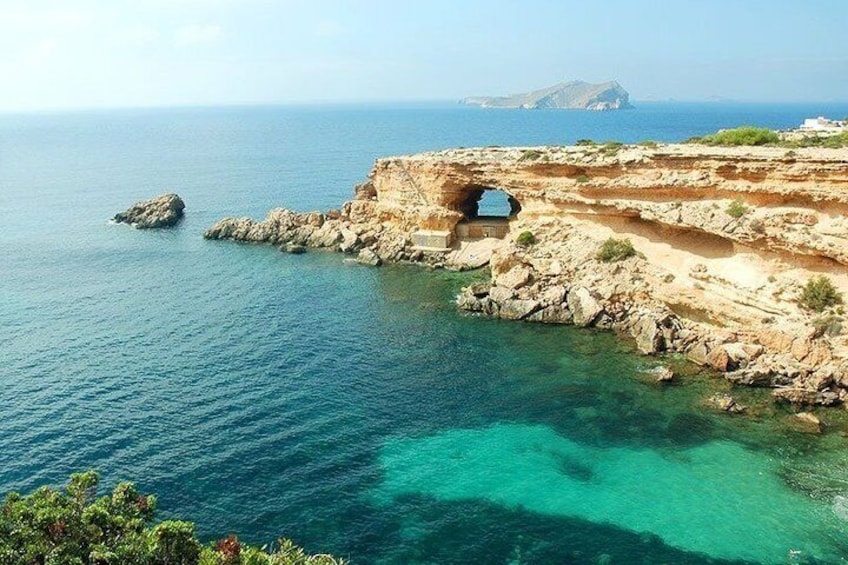 Un paysage côtier avec une formation rocheuse, des eaux turquoise et limpides, et une île qui se profile à l’horizon. 3