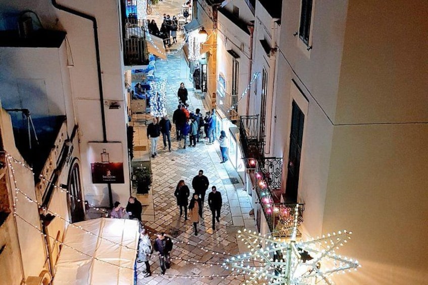 Eine schmale Straße mit Fußgängern, Gebäuden an beiden Seiten und einer dekorativen Lichtkonstruktion im Vordergrund. 4