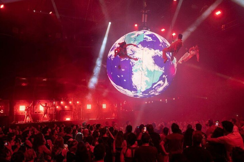 A crowd at a concert with a large globe and performers on it. 1