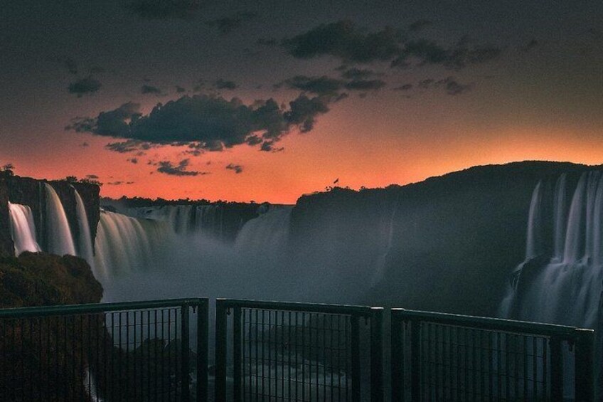 A waterfall with a metal railing in the foreground. 3
