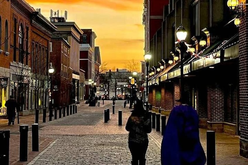A cobblestone street lined with brick buildings, street lamps, and a sunset sky. 3