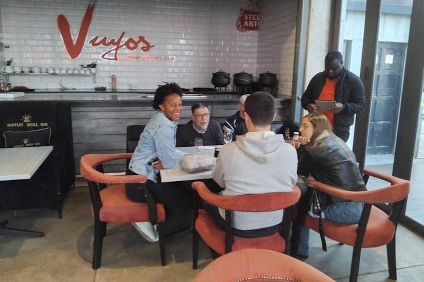 Eine Gruppe von Personen sitzt an einem Tisch in einem Restaurant mit modernem Interieur, darunter eine Backsteinwand und eine Speisekarte. 2