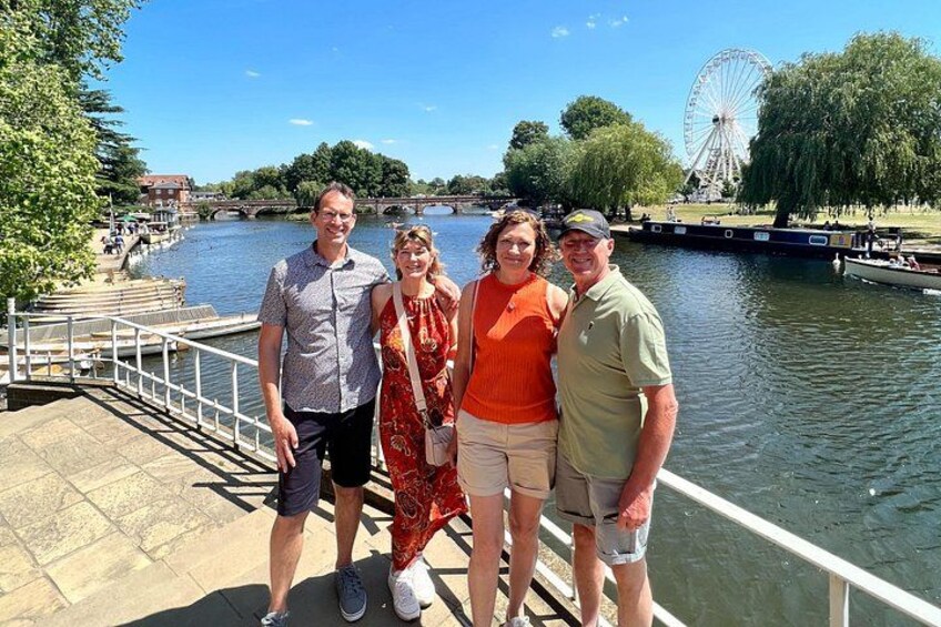A group of people standing by a river with a Ferris wheel in the background. 1