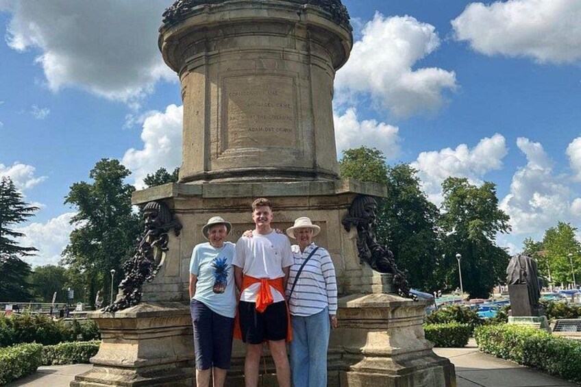 A group of people standing in front of a large stone monument with inscriptions, surrounded by greenery and a clear sky. 5