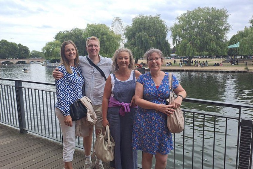 A group of people standing on a wooden boardwalk by a river with trees and a Ferris wheel in the background. 3