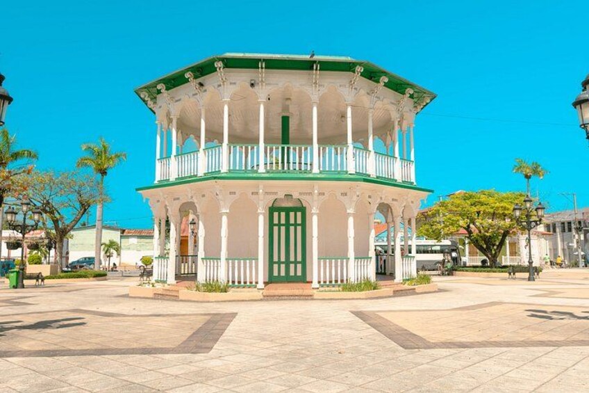 A white building with green accents and a balcony, surrounded by a paved square. 3