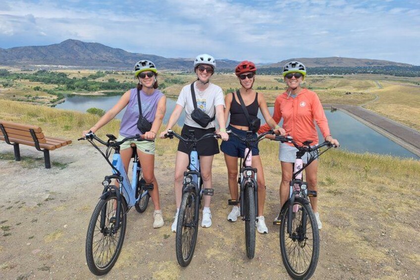 Cuatro personas en bicicleta, un banco y un lago en un paisaje montañoso. 2