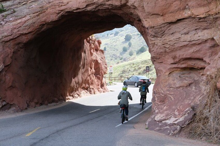 Una carretera que atraviesa un gran arco de roca con ciclistas pedaleando. 4