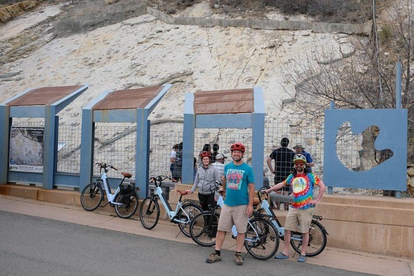 Un grupo de personas junto a bicicletas, una zona arenosa y una valla metálica. 2