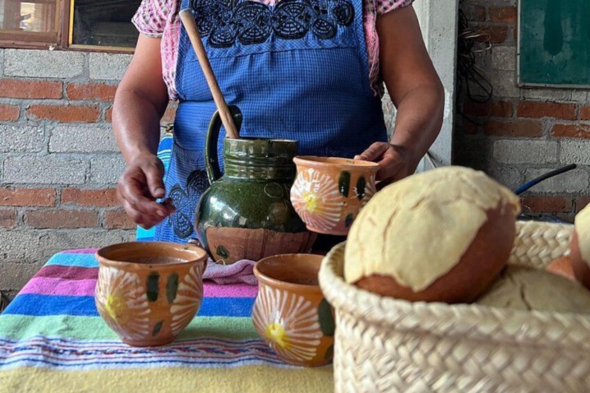 A person preparing food with a green pot and ceramic cups on a table with a woven basket. 3