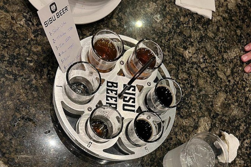 A tray with five glasses of beer, a menu, and a partially visible bottle on a granite countertop. 2