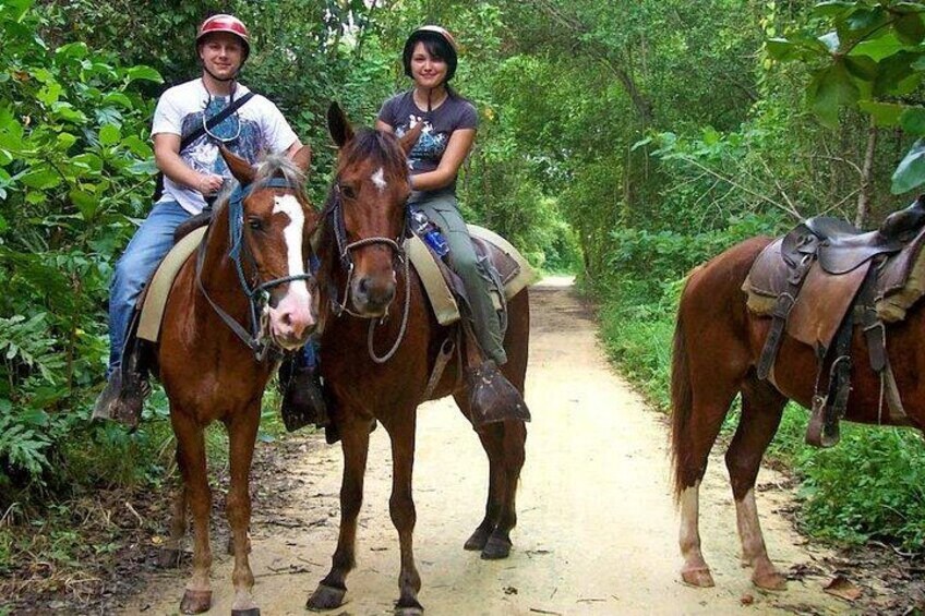 Two people riding horses on a dirt path surrounded by greenery. 3