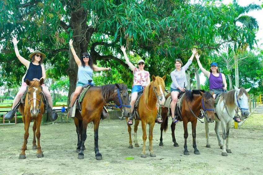 A group of people riding horses in an outdoor setting with trees and a dirt ground. 3