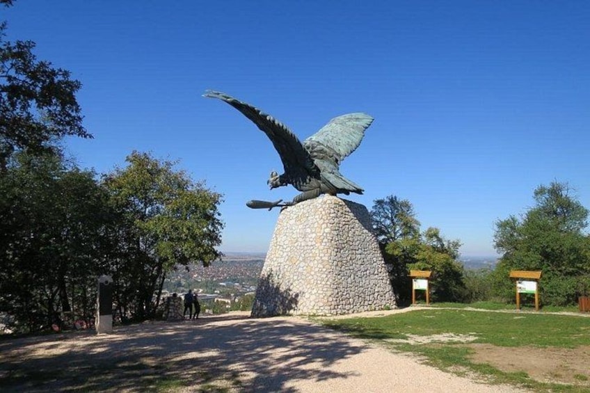 Eine große Vogel-Skulptur auf einem Steinsockel, umgeben von Bäumen und wolkenlosem Himmel. 5