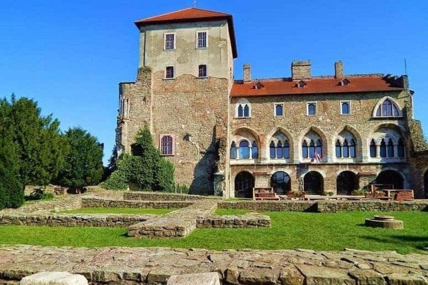 Ein historisches Steinhaus mit einem Turm und Bogenfenstern, umgeben von einem gepflegten Rasen und einem Steinweg. 3