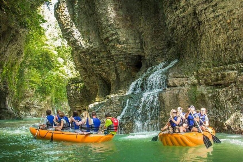 Two groups of people rafting on a river with a waterfall in a rocky canyon. 1