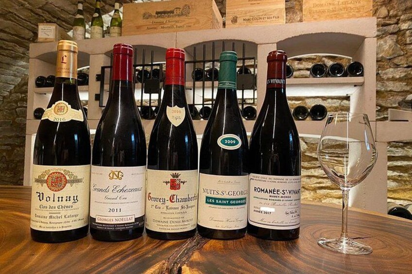 A selection of wine bottles on a wooden table with a wine glass to the side. 3