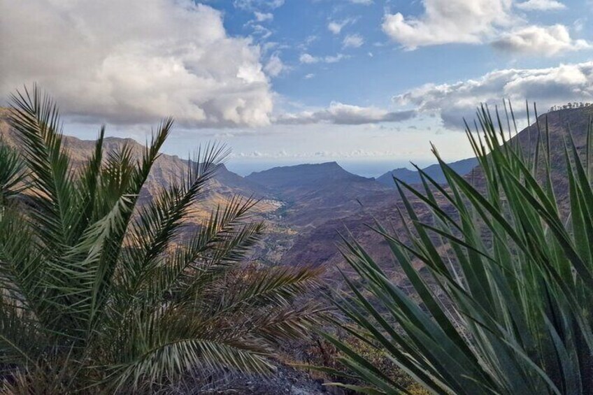 A mountainous landscape with green vegetation in the foreground and a view of distant mountains under a partly cloudy sky. 4