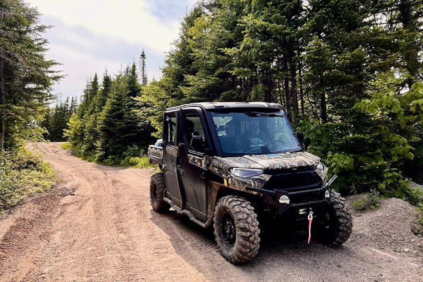 A black off-road vehicle on a dirt path surrounded by dense forest. 1